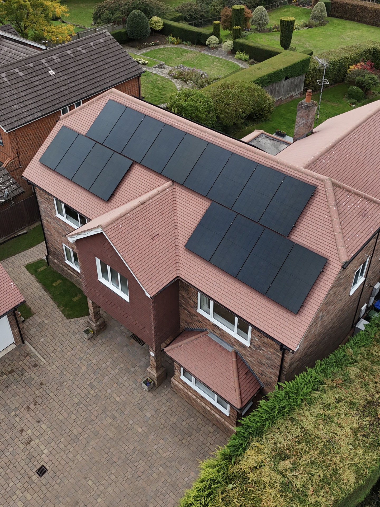 Aerial view of a red-brick detached home with rooftop solar panels installed by MJ Renewables